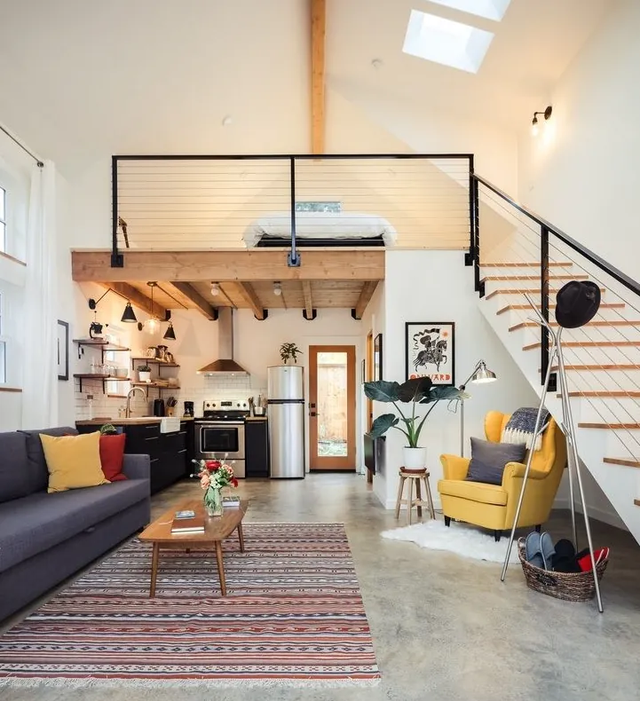 ADU living room with a sofa and rug, an open stair and a loft bedroom over the kitchen