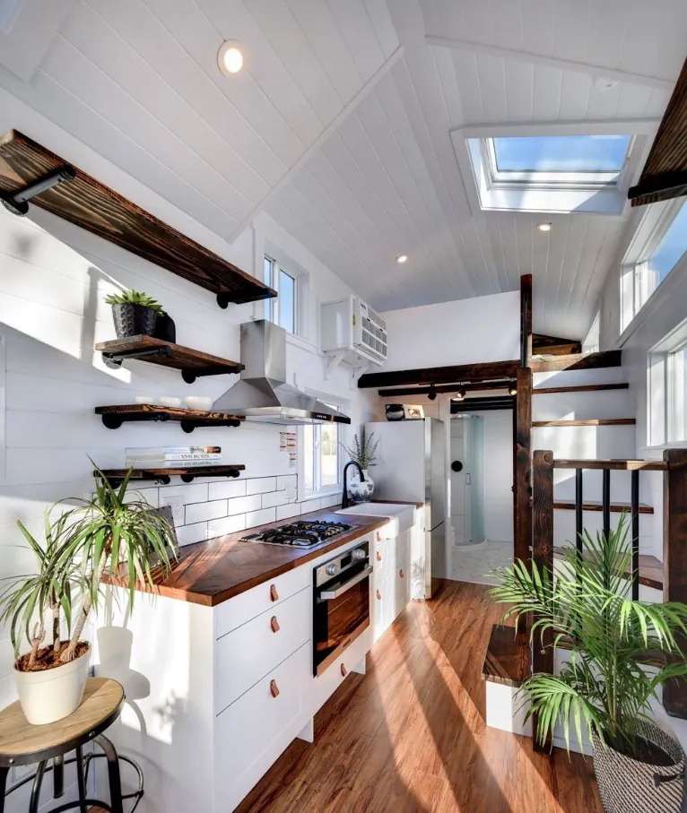 Bright tiny home kitchen with butcher-block counters, open shelving and a sleeping loft above